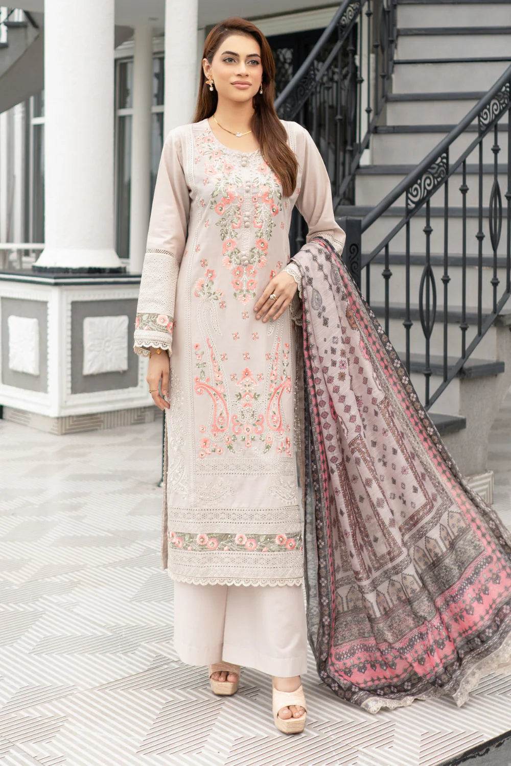Woman in a light-colored embroidered suit with a dupatta standing on a porch.
